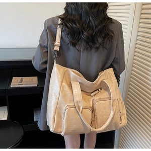 Detail of large beige tote bag with crocodile texture and multi-pocket design on model