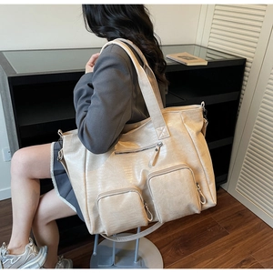 Detailed close-up of beige tote bag with crocodile pattern and multi-pocket zippers