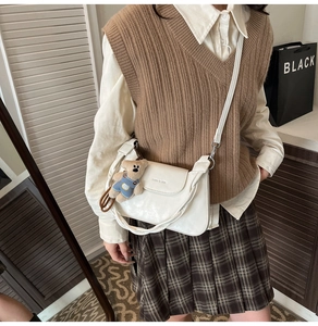 Side view of a white leather crossbody bag featuring a cute plush bear charm detail