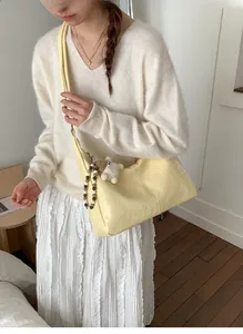 Detail of light yellow crescent bag featuring pleated texture and cute sheep charm pendant