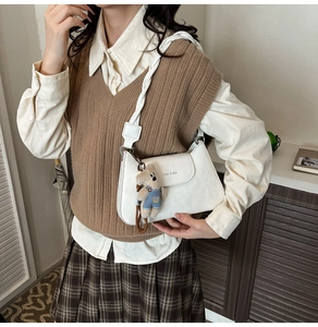 Detail of white leather shoulder bag with woven strap and cute bear pendant accessory