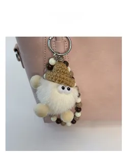 Détail d'un bijou de sac en peluche blanche avec bonnet au crochet sur un sac à main rose