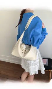 Detail view of cream pleated underarm bag with plush ball charm on a blue sweater