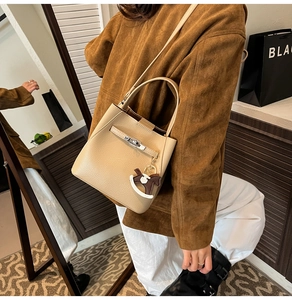 Close-up of beige lychee leather bucket bag with metal buckle and horse charm detail