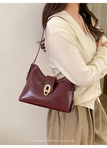 Close-up of retro wine red shoulder bag with glossy leather and golden oval metal clasp