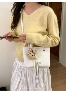 Detail of white leather handbag featuring a cute teddy bear charm and silver logo text