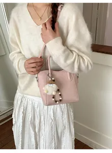 Détail du sac seau en cuir rose avec charm en peluche et perles sur tenue blanche