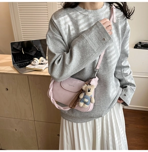Pink leather crossbody bag detail with cute bear charm and woven handle in lifestyle setting