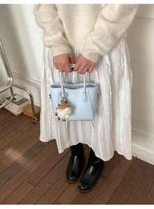 Détail d'un sac seau en cuir bleu clair avec un porte-clé en peluche et poignées rondes