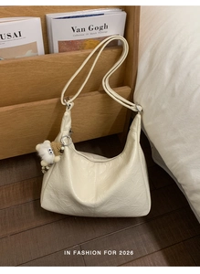 Detail of creamy white pleated hobo bag with a cute plush sheep charm in a cozy room