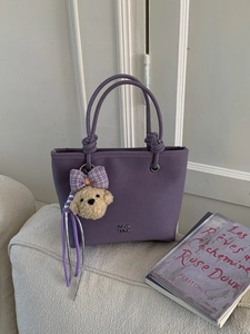 Minimalist purple matte leather tote bag with knotted handles and puppy charm on a sofa