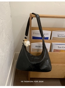 Detail of black glossy oiled leather hobo bag with plush charm on artistic wooden shelf