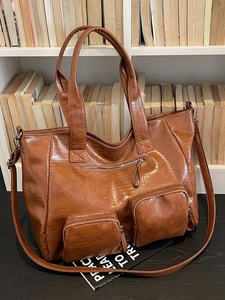Brown crocodile texture large tote bag with front zipper pockets on a bookshelf