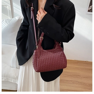 Detail of burgundy woven leather handbag with adjustable strap and gold buckle