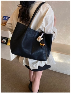 Vue latérale du grand sac cabas noir avec breloque fleur portée à l'épaule du mannequin