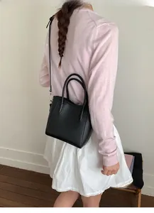 Détail d'un sac seau en cuir noir porté par un mannequin avec une fine bandoulière