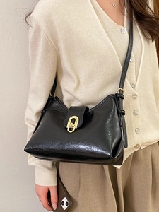 Chic black polished leather crossbody bag with a distinctive golden oval rotating clasp