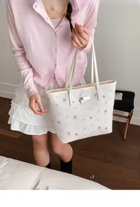 Detail of white tote bag with pink cartoon bear prints and silver heart charm accessory
