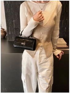 Detail of minimalist black crocodile pattern handbag paired with a beige knit vest