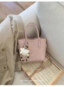 Sac seau rose en cuir avec pendentif peluche mignon sur un canapé beige doux