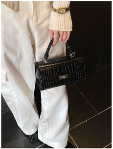 Detail showing shiny black crocodile embossed leather texture and silver metal twist lock