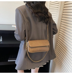 Detail of vintage brown leather baguette bag with gold chain strap on grey blazer