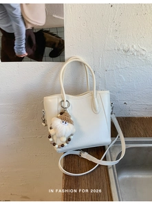 Détail du sac cabas blanc grainé avec un pendentif poupée mignon sur un bureau en bois