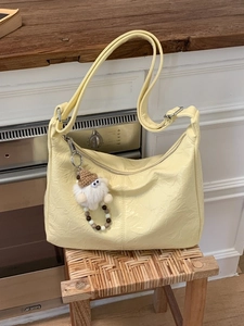 Yellow vintage pleated hobo tote bag with a white plush doll charm in a home setting