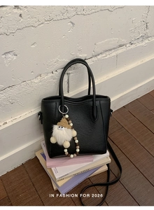 Détail d'un sac seau noir en similicuir mat avec pompon sur des magazines de mode