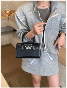 Close-up of black leather crossbody square bag with silver clasp on a grey outfit