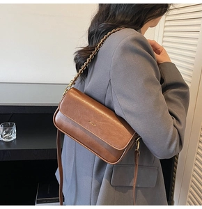 Detailed close-up of brown leather baguette bag with gold logo and metal chain strap