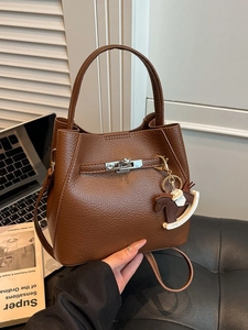 Brown leather bucket bag with horse charm held against an office desk background