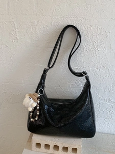Black crinkled patent leather tote bag with a cute plush doll charm on a white stand
