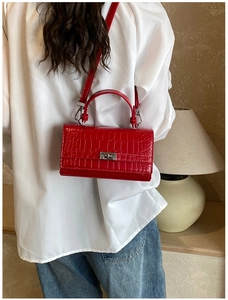 Detail of red crocodile texture crossbody bag with silver lock worn by model on white shirt