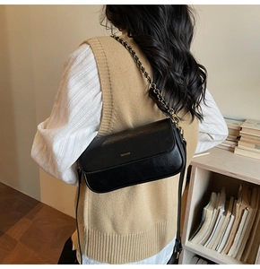 Detailed view of black leather baguette bag with gold chain strap and metal hardware