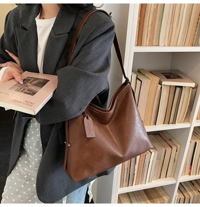 Brown leather tote bag styled with a grey blazer against a bookshelf backdrop