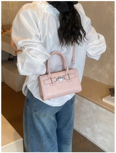 Close-up of light pink crossbody bag with decorative silver heart buckle and top handle