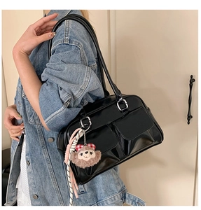 Detail of black glossy shoulder bag with dual front pockets and plush bear charm accent