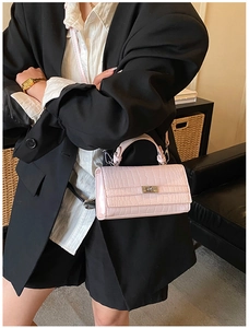 Detail of pink crocodile embossed leather handbag with metal buckle worn by model