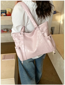 Detail of a large pink faux leather tote bag with drawstring side and dual shoulder straps