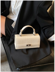 Close-up of white crocodile pattern handbag with metal turn-lock on black suit