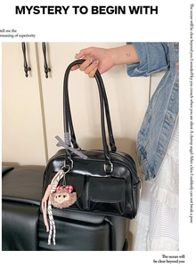 Detail of black faux leather shoulder bag with plush charm and bow decoration