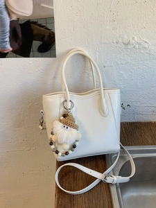 Sac seau minimaliste en similicuir beige avec pendentif peluche sur table en bois