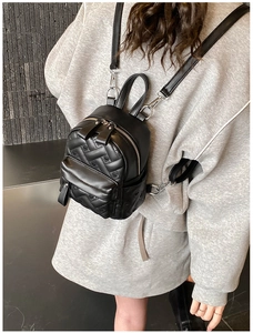 Detail of heart-quilted black leather mini backpack with silver zipper on model