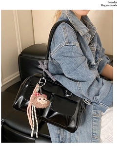 Detail of black glossy Boston bag with plush charm and ribbon on model's shoulder