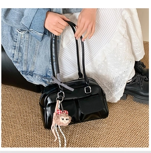 Detail of black glossy shoulder bag featuring double pockets and cute plush charm