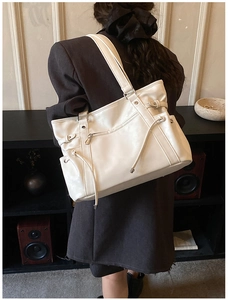 Close-up of off-white tote bag with side drawstrings and front zipper detail