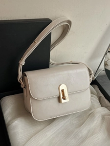 Elegante borsa beige con chiusura rotante dorata su sfondo di seta bianca