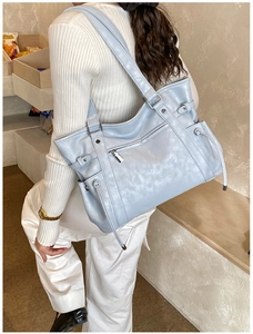 Detail of light blue faux leather tote bag with zip pocket shown on female model