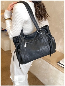 Side view of a large black tote bag with silver hardware on a female model shoulder